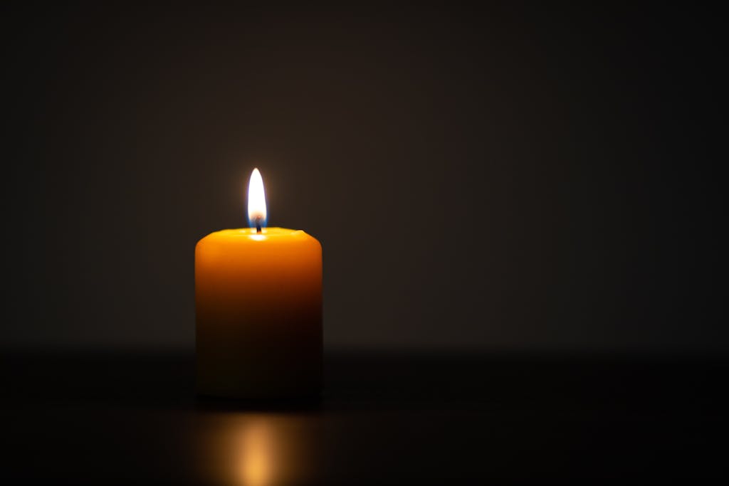 Single candle glowing softly in a dark space, representing remembrance and reflection.